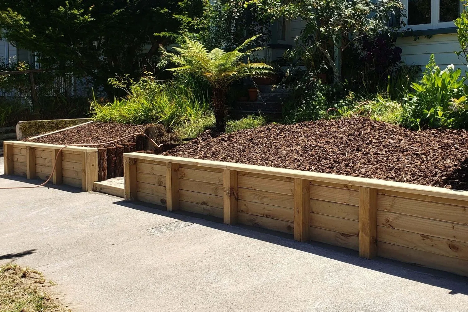 Timber retaining wall bordering a mulched garden bed and driveway